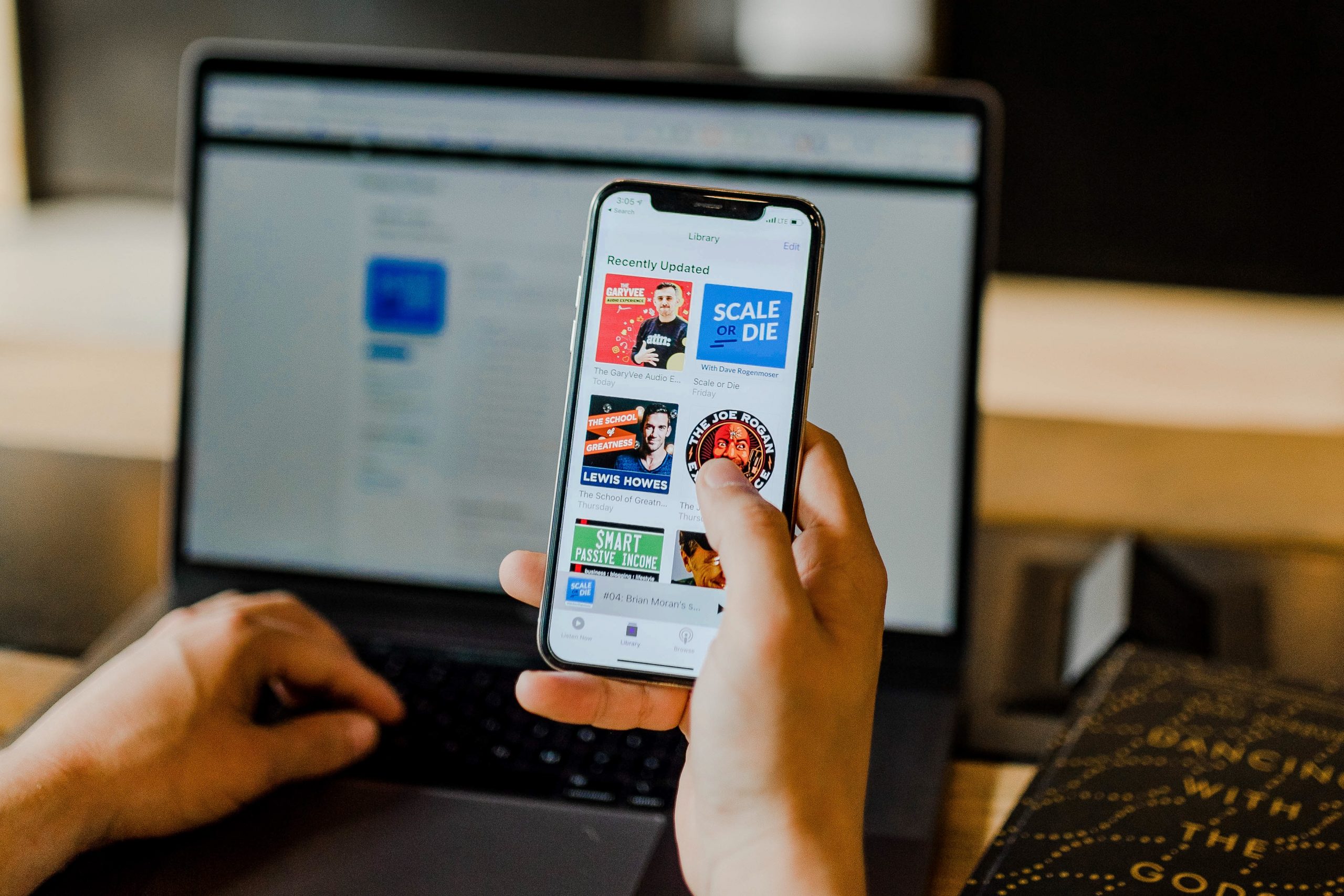 Someone holding a phone with a selection of podcasts on the screen.